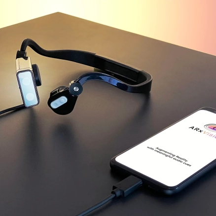 The ARx Headset sits on a table next to a smart phone with the ARxVision app open.